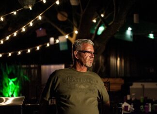 Ralph Philbaum sitting in a cantina, surrounded by colorful artwork and a bottle of tequila on the table.