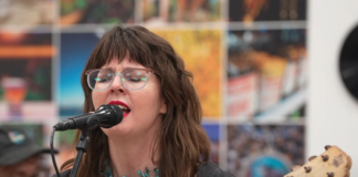Lara Ruggles, known as Sharkk Heartt, performing live on stage in Tucson, smiling as she sings and plays guitar.
