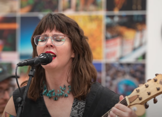Lara Ruggles, known as Sharkk Heartt, performing live on stage in Tucson, smiling as she sings and plays guitar.