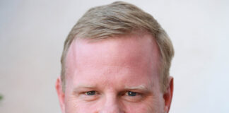 Tom Heath smiling into the camera, wearing a navy blue blazer.