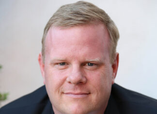 Tom Heath smiling into the camera, wearing a navy blue blazer.