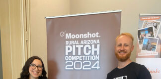 Chelsea Alder and Jason Robinson standing in front of a Pitch Competition 2024 poster, with Chelsea holding a Timber Tote product.