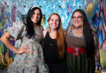 Three Tucson muralists pose in front of the colorful Threads of Tucson, Woven by Women mural in El Presidio.