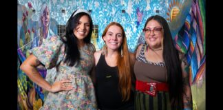 Three Tucson muralists pose in front of the colorful Threads of Tucson, Woven by Women mural in El Presidio.