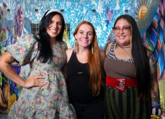 Three Tucson muralists pose in front of the colorful Threads of Tucson, Woven by Women mural in El Presidio.